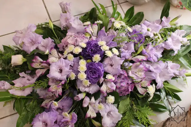 Klasszikus kialakítású sírcsokor lila színű virágokkal, örök zöldekkel és vízutánpótlással növényeknek. A búcsú személyesebbé tehető, ha kegyeleti csokorba kéred elhunyt kedvenc virágait.